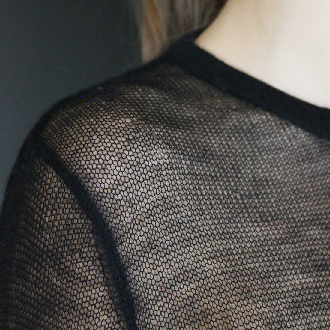 Close-up of a fine-gauge cashmere and silk knit, showing the semi-sheer drop-needle net across the shoulder